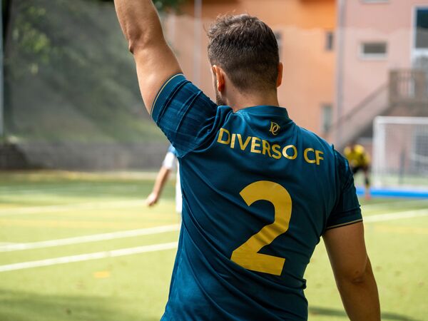 Záda dresu s nápisem DIVERSO CF a číslem 2, hráč hlásí zdviženou rukou